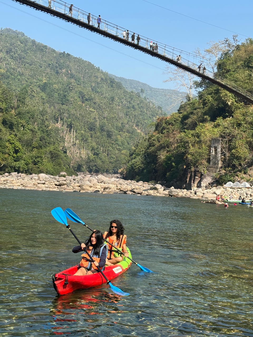 Travelers kayaking below a suspension bridge in Meghalaya